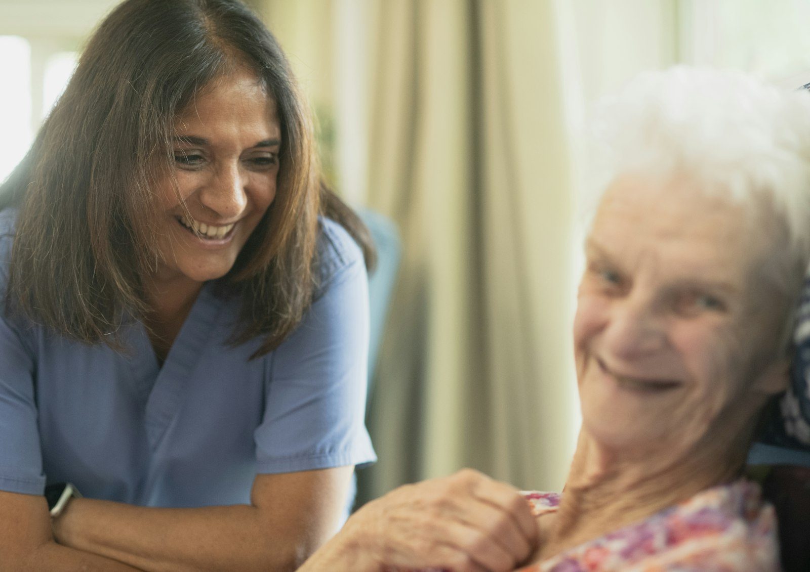 A carer sharing a laugh with an elderly woman at home
