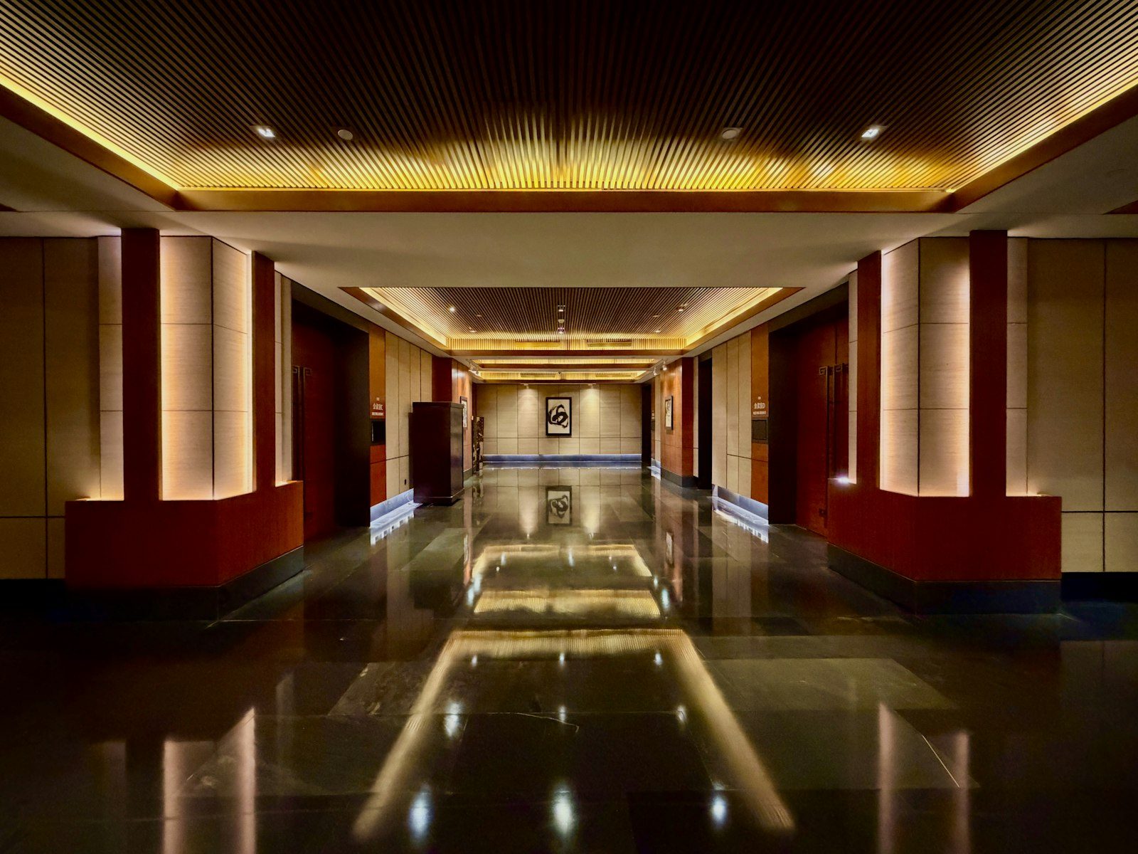 A warmly lit hotel corridor with polished stone floor